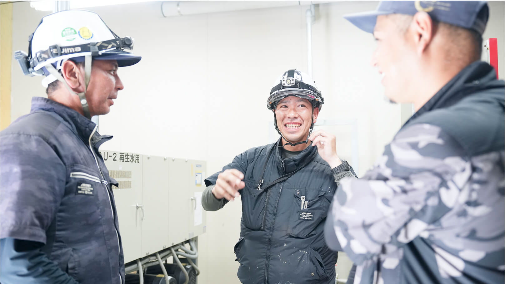 複数の作業員が現場で笑顔で会話しており、職場の明るい雰囲気が伝わる場面
