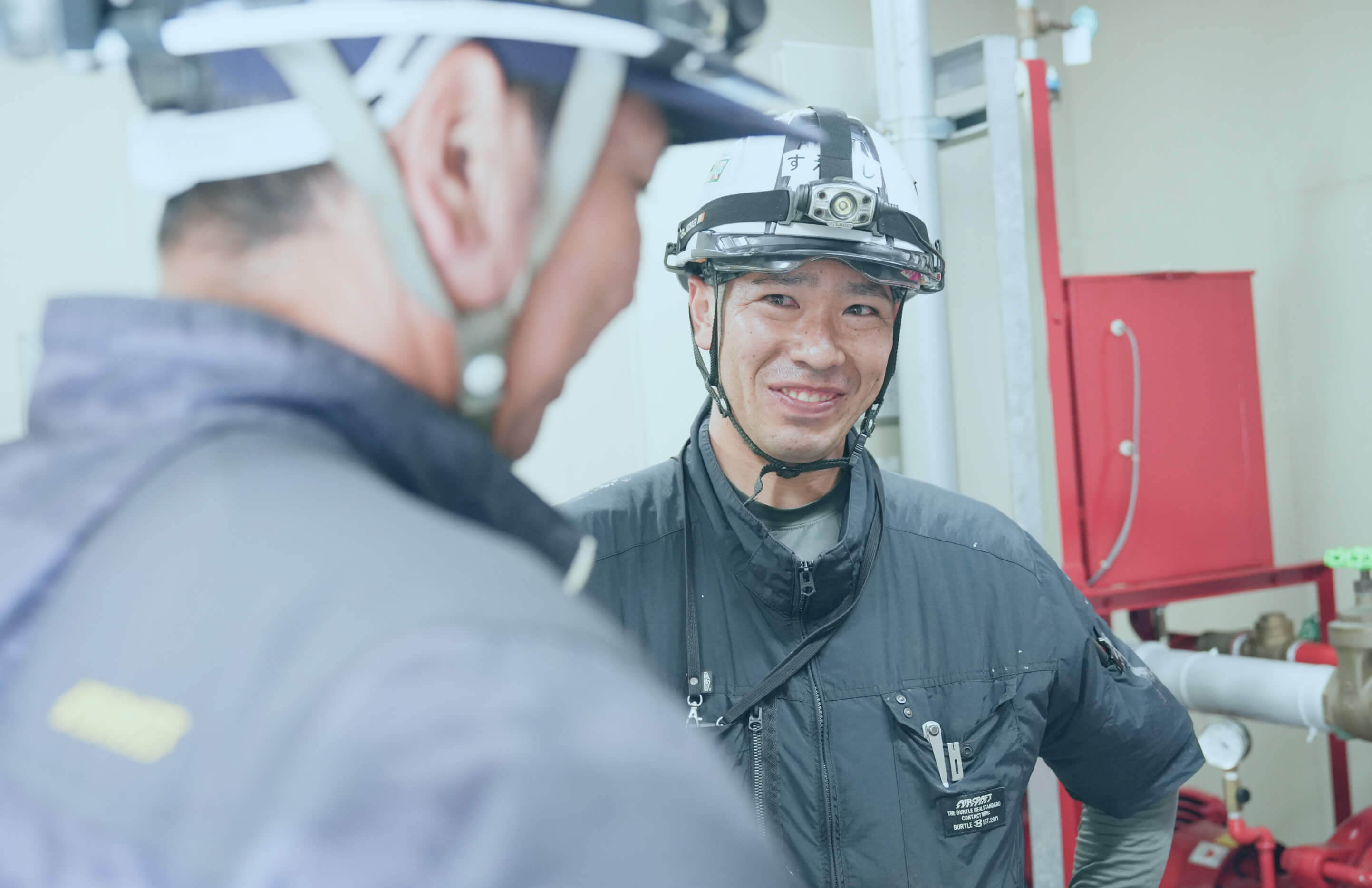 安全ヘルメットを着用した作業員が仲間と笑顔で会話している場面
